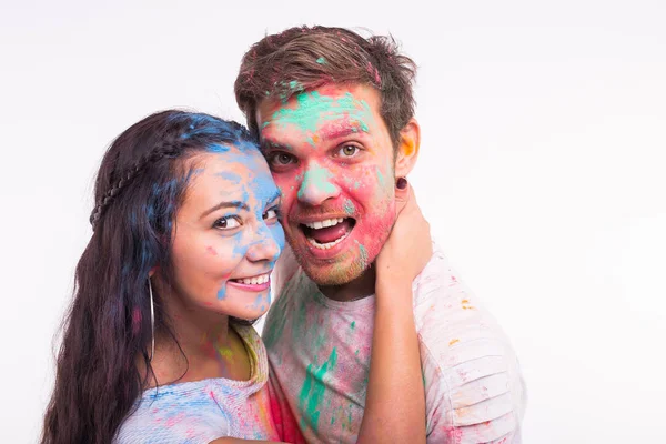 Концепция праздников, холи и людей - улыбающиеся смешные женщина и мужчина позируют с разноцветным порошком на их лицах на белом фоне — стоковое фото