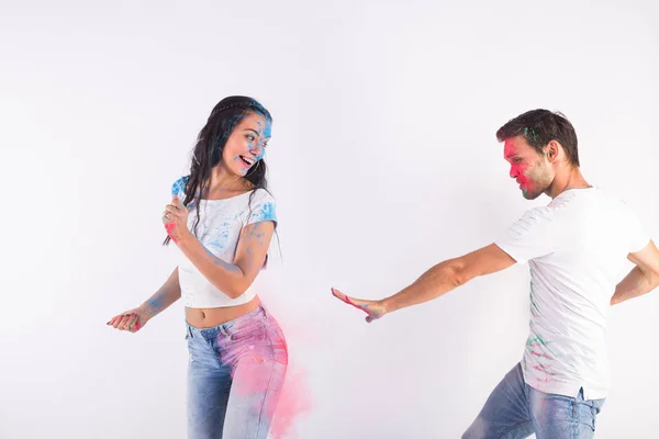 Conceito de férias, holi e pessoas - Casal feliz se divertindo com pó multicolorido em seus rostos no fundo branco — Fotografia de Stock