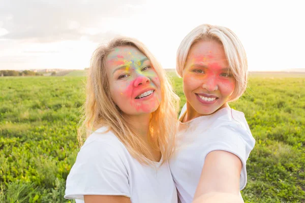 Festival indio de holi, concepto de personas - dos mujeres jóvenes tomando selfie con polvo colorido en las caras —  Fotos de Stock