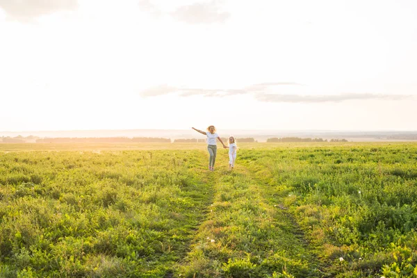 Familia, verano y concepto de vacaciones - Madre sosteniendo a sus hijas de la mano corriendo en el campo verde — Foto de Stock