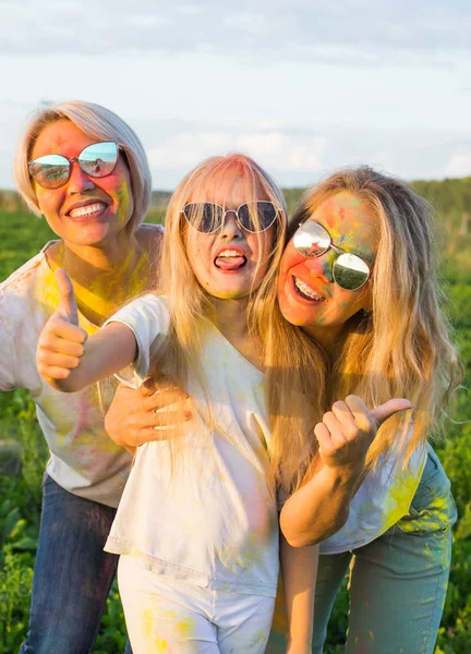 Vacaciones, fiesta holi y concepto familiar - Chicas felices y divertidas cubiertas de pintura en verde gesto de campo pulgares hacia arriba —  Fotos de Stock