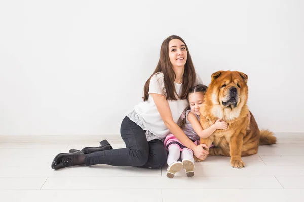 Mascotas, niños y concepto familiar - Niña y su madre abrazando perro chow-chow sobre fondo blanco — Foto de Stock