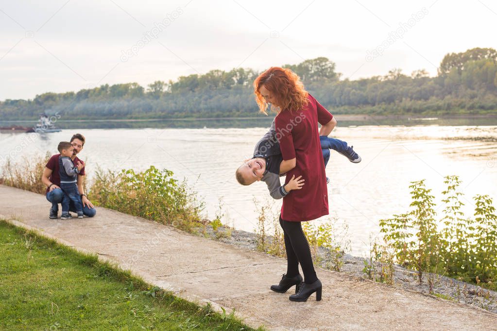Family and children concept - mother, father and two sons enjoying the summer time, playing near the river