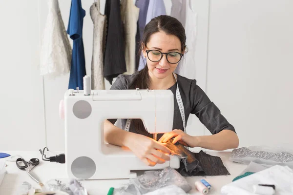 people, fashion and showroom concept - young fashion designer sews clothes on a sewing machine