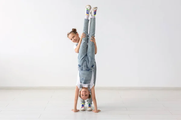 Concepto de familia y deporte - Dos chicas gemelas acróbatas están de pie en las manos sobre el fondo blanco — Foto de Stock