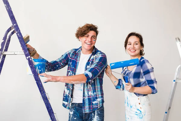 Repair, renovation and love couple concept - young family doing redecoration and painting walls together and laughing. — Stock Photo, Image