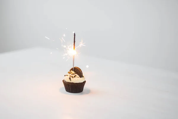Food, bakery, holiday, happy birthday and desserts concept - delicious cupcake with sparkler and cookie on white table with copy space — Stock Photo, Image