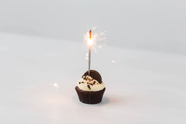 Food, holidays, happy birthday, bakery and desserts concept - delicious cupcake with sparkler on white table.