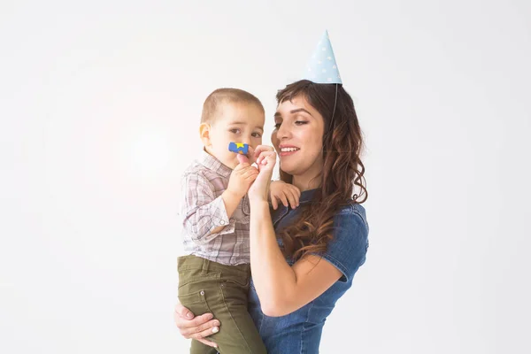 Concepto de niños, familia y vacaciones - madre joven en sombrero de cumpleaños sosteniendo al pequeño hijo sobre un fondo blanco — Foto de Stock