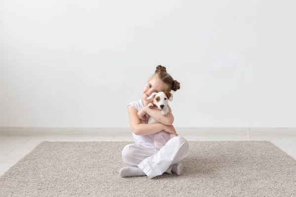 Concepto de personas, niños y mascotas - niña pequeña sentada en el suelo con un lindo cachorro Jack Russell Terrier — Foto de Stock