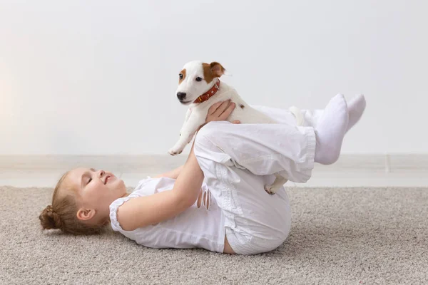 people, children and pets concept - little kid girl lying on the floor with cute puppy in hands