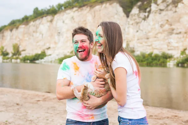 Festival holi, vacanze, turismo, pet e natura concetto - Ritratto di donna e uomo con gatto coperto polvere multicolore — Foto Stock