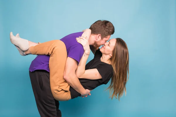 Gente, relación y concepto divertido - Hombre sonriente sosteniendo hermosa mujer sobre fondo azul — Foto de Stock