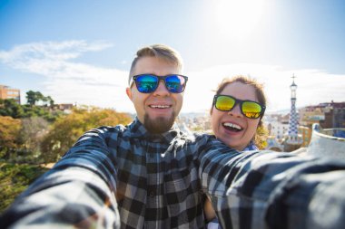Komik genç çift kamera ile akıllı telefon Park Guell, Barselona, İspanya, gülümseyen fotoğrafı çekmek.