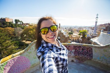 Seyahat ve tatil kavramı - kamera çekimi fotoğraf Park Guell, Barselona, İspanya, gülümseyen akıllı telefon ile arayan güzel genç kadın.
