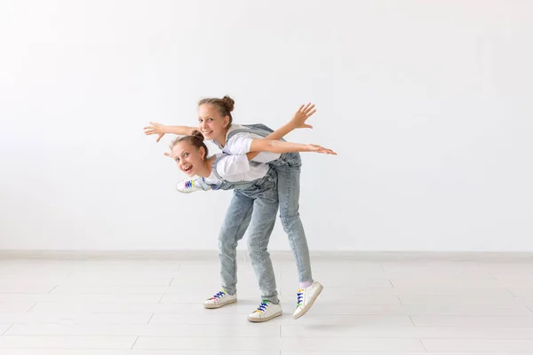 people, children and family concept - little girl carrying her twin sister piggyback on white background