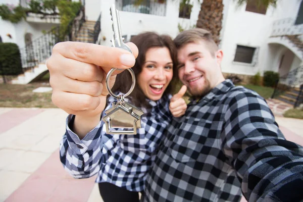 Concepto de bienes raíces y propiedades - Pareja feliz sosteniendo las llaves de un nuevo hogar y casa en miniatura —  Fotos de Stock