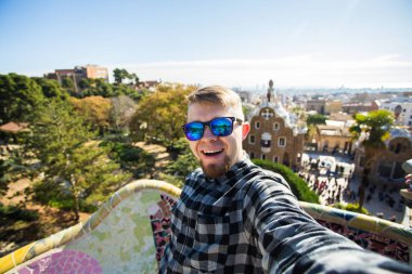 Seyahat ve tatil kavramı - yakışıklı adam akıllı telefon Park Guell, Barselona, İspanya, gülümseyen ile kamera çekimi fotoğrafa bakan.