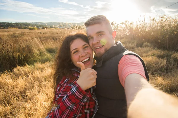 Resor, turism och natur koncept - leende par tar selfie på fältet och visar tummen — Stockfoto