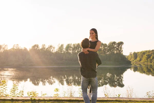 Romantický, lidé a letní koncept - muž zvedl ženu v náručí poblíž jezera na západ slunce — Stock fotografie