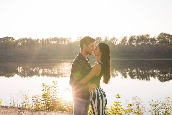 Романтика, любовь, люди концепция - молодая пара, обнимающаяся у озера на закате — стоковое фото