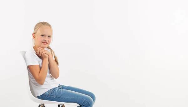 Adorable niña pequeña con el pelo largo y rubio sentado en la silla sobre fondo blanco — Foto de Stock