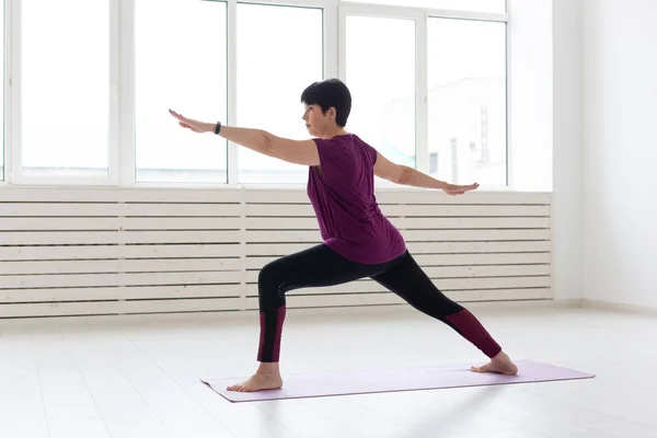 Gente, yoga, deporte y concepto de salud - Mujer de mediana edad de pie en Warrior sobre fondo blanco —  Fotos de Stock