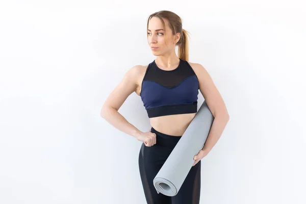 Concepto de personas, fitness y deporte - Mujer atractiva y saludable sosteniendo alfombra gris sobre fondo blanco — Foto de Stock