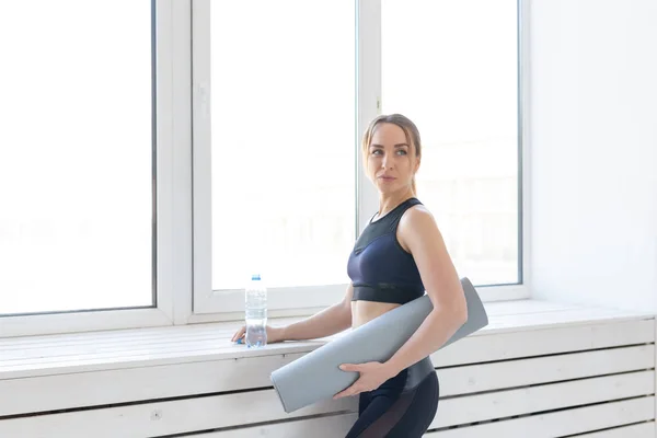 Yoga, concepto saludable y deportivo - Mujer en forma joven sosteniendo alfombra gris y botella de agua — Foto de Stock