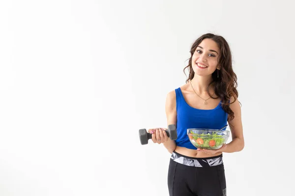 Deporte, estilo de vida saludable, concepto de personas - mujer morena joven con ensalada y una mancuerna. Ella sonríe y disfruta del estilo de vida saludable —  Fotos de Stock