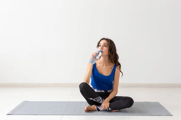 Estilo de vida saludable, personas y concepto de deporte - Mujer sonriente sentada en la esterilla de yoga y agua potable después del entrenamiento duro —  Fotos de Stock