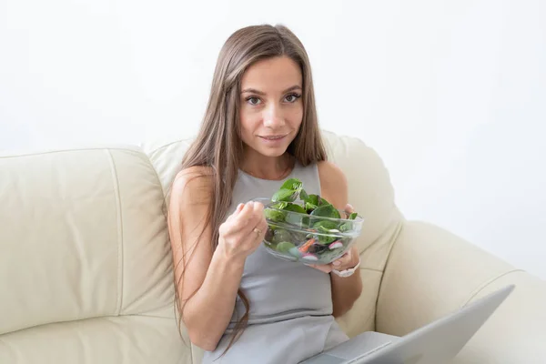 Mode de vie sain, bonne alimentation, se détendre et les gens concept- jeune belle femme assise sur le canapé blanc et de manger une salade — Photo