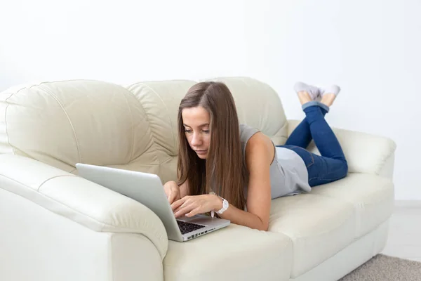 Технологии, отдых и внештатная концепция - красивая молодая женщина лежит на диване и работает на ноутбуке — стоковое фото