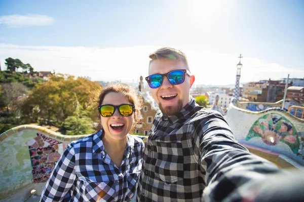 Смішні молода пара дивиться на камеру прийняття фото з смарт-телефону, посміхаючись в парк Гуель, Барселона, Іспанія. — стокове фото