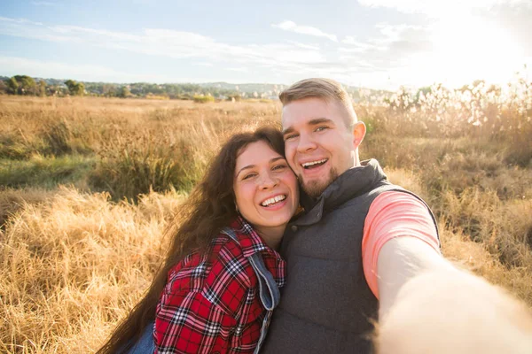 Reise-, Urlaubs- und Urlaubskonzept - glückliches Paar macht Selfie vor Hintergrund auf dem Feld und Sonnenuntergang — Stockfoto