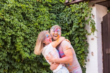 Tatil, bayram ve insanlar kavramı - mutlu çift yüzlerinde çok renkli toz ile eğleniyor