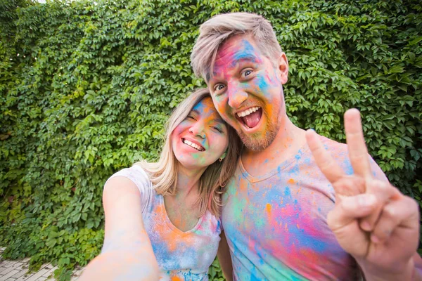 Holiday, holi and people concept - Woman and man with painted faces taking selfie over bush backgrund — Stock Photo, Image