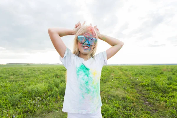 Barn, festival av holi och helgdagar koncept - glad liten flicka täckt med färg pulver leende över naturen bakgrund — Stockfoto