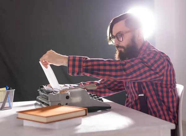 Gente y concepto de tecnología - Día Mundial del escritor, hombre guapo con barba trabajando en la máquina de escribir sobre fondo negro — Foto de Stock