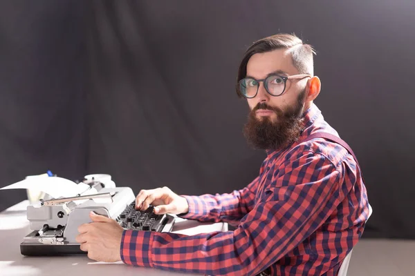 Concepto de personas y tecnología - Hombre guapo de vista lateral con barba trabajando en máquina de escribir sobre fondo negro — Foto de Stock