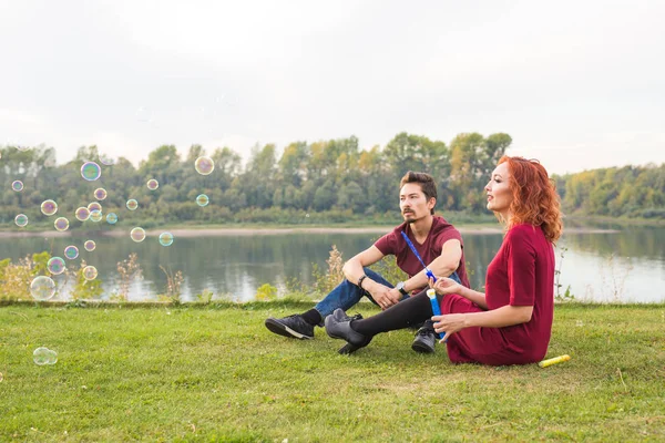 Familie, Menschen Konzept - junges Paar pustet Seifenblasen in der Nähe des Flusses — Stockfoto