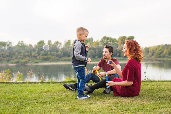 Familjen och naturen koncept - mamma, pappa och deras barn som leker med färgglada såpbubblor — Stockfoto