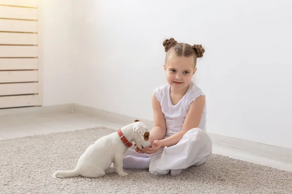 Concepto de niños, mascotas y animales: niña pequeña en pijama jugando con el cachorro Jack Russell Terrier en el suelo — Foto de Stock