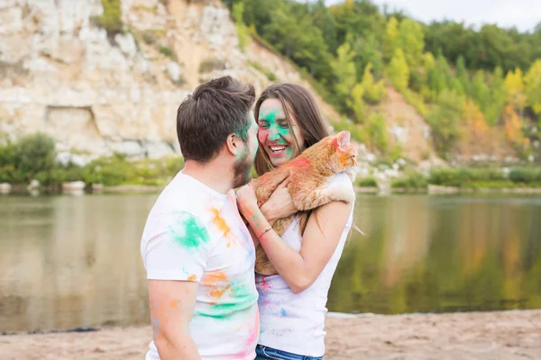 节日洞, 节日, 旅游和自然概念-夫妇穿着白衬衫抱着猫, 覆盖着五颜六色的灰尘 — 图库照片