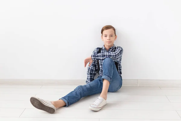 Adolescente, niños y concepto de moda - Muchacho de moda sentado en el suelo sobre fondo blanco — Foto de Stock