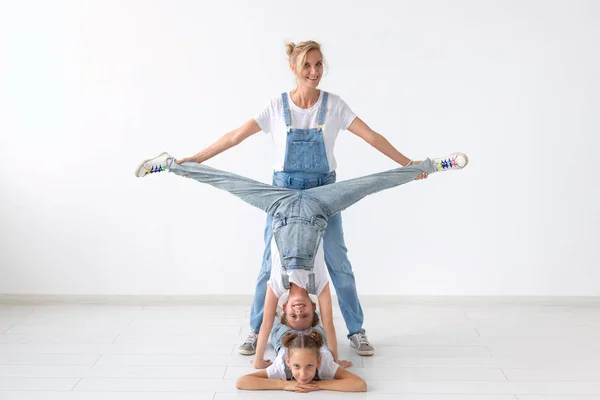 Люди, семейная и спортивная концепция - молодая мама с близнецами дочери делают упражнения на белом фоне — стоковое фото