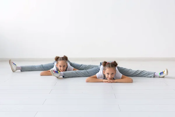 Pessoas, crianças e conceito acrobático - pequenas irmãs gêmeas fazendo exercícios em fundo branco — Fotografia de Stock