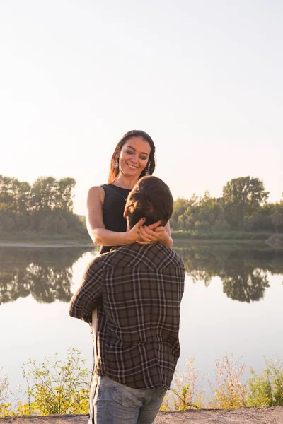 Romântico, pessoas e conceito de verão - homem levantou uma mulher em seus braços perto do lago ao pôr do sol — Fotografia de Stock