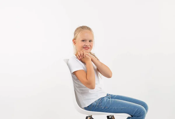 Alegre niña rubia pequeña sentada en la silla con sonrisa aislada sobre fondo blanco — Foto de Stock