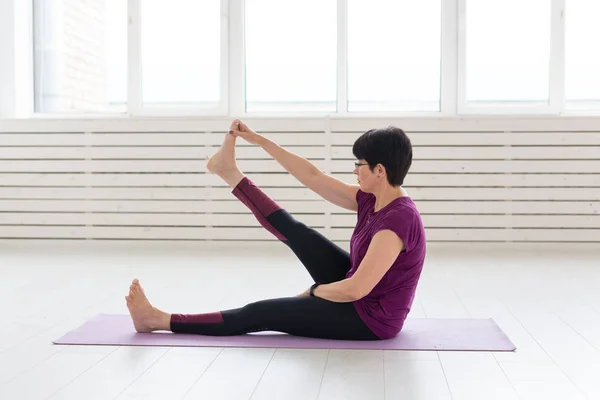 Yoga, concepto de personas - una mujer de mediana edad haciendo un yoga y tratar de hacer una asana —  Fotos de Stock